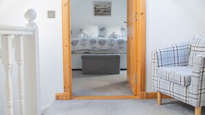 A bedroom with a bed, a grey bench, a plaid chair, and a white railing. - Ben Edra Croft by Interhome (North Skye)