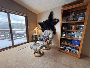 A room with a large window, a chair with a stuffed animal, a bookshelf, and a wall-mounted bear decoration. - Cozy Mountain Escape with Fireplace, Views, Balcony & Easy Ski Access (Durango)