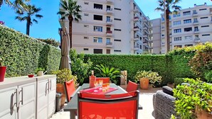 An outdoor patio with a table and chairs, surrounded by greenery and a high-rise building in the background. - Le Chaville by Interhome (Cagnes-sur-Mer)