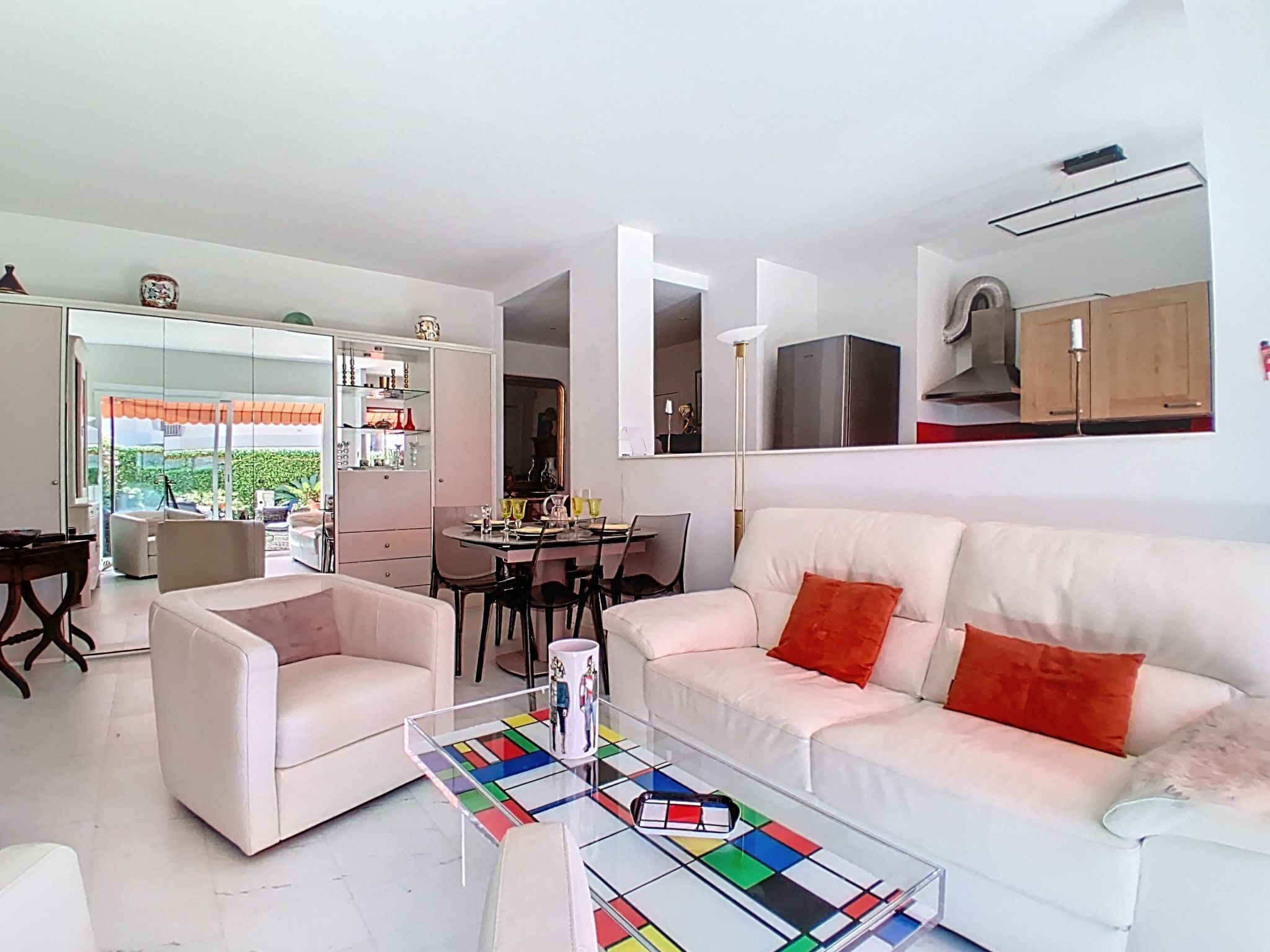 Uma sala de estar moderna com um sofá branco, uma mesa de centro de vidro e uma área de jantar com mesa e cadeiras brancas.