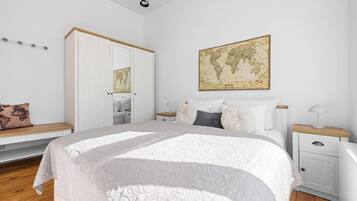 Een slaapkamer met een groot bed, een garderobe, een nachtkastje, een lamp, een kaart aan de muur, en een bankje met een kussen.