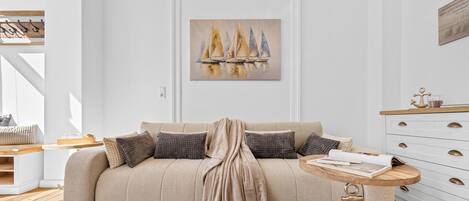 A neutral-toned living room with a sofa, a coffee table, and a painting of sailboats.