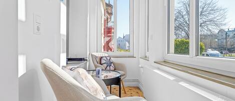 Une pièce avec une grande fenêtre, une chaise, une petite table et un radiateur.