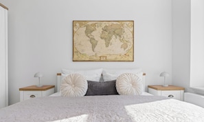 Quarto com uma cama, duas mesas de cabeceira, uma pintura de um mapa-múndi e uma parede branca.