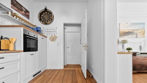 A kitchen with white cabinets, a wooden floor, and a clock on the wall. - Steuerbord - own parking space, in the city, roller shutters, ground floor (Flensburg)