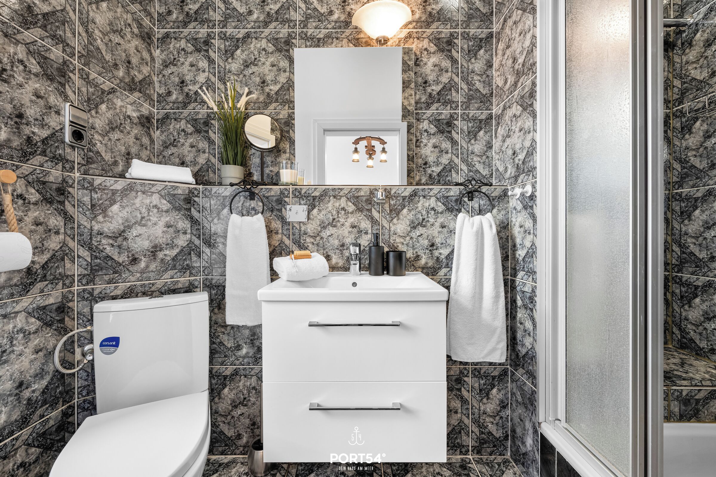 Ein Badezimmer mit Toilette, Waschbecken und Dusche. Die Wände sind mit einem Marmormuster gefliest.