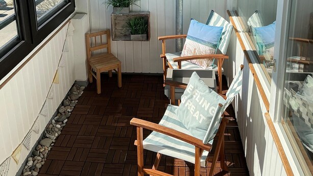 Ein Balkon mit Holzstühlen, einem kleinen Tisch und Pflanzen in Töpfen.
