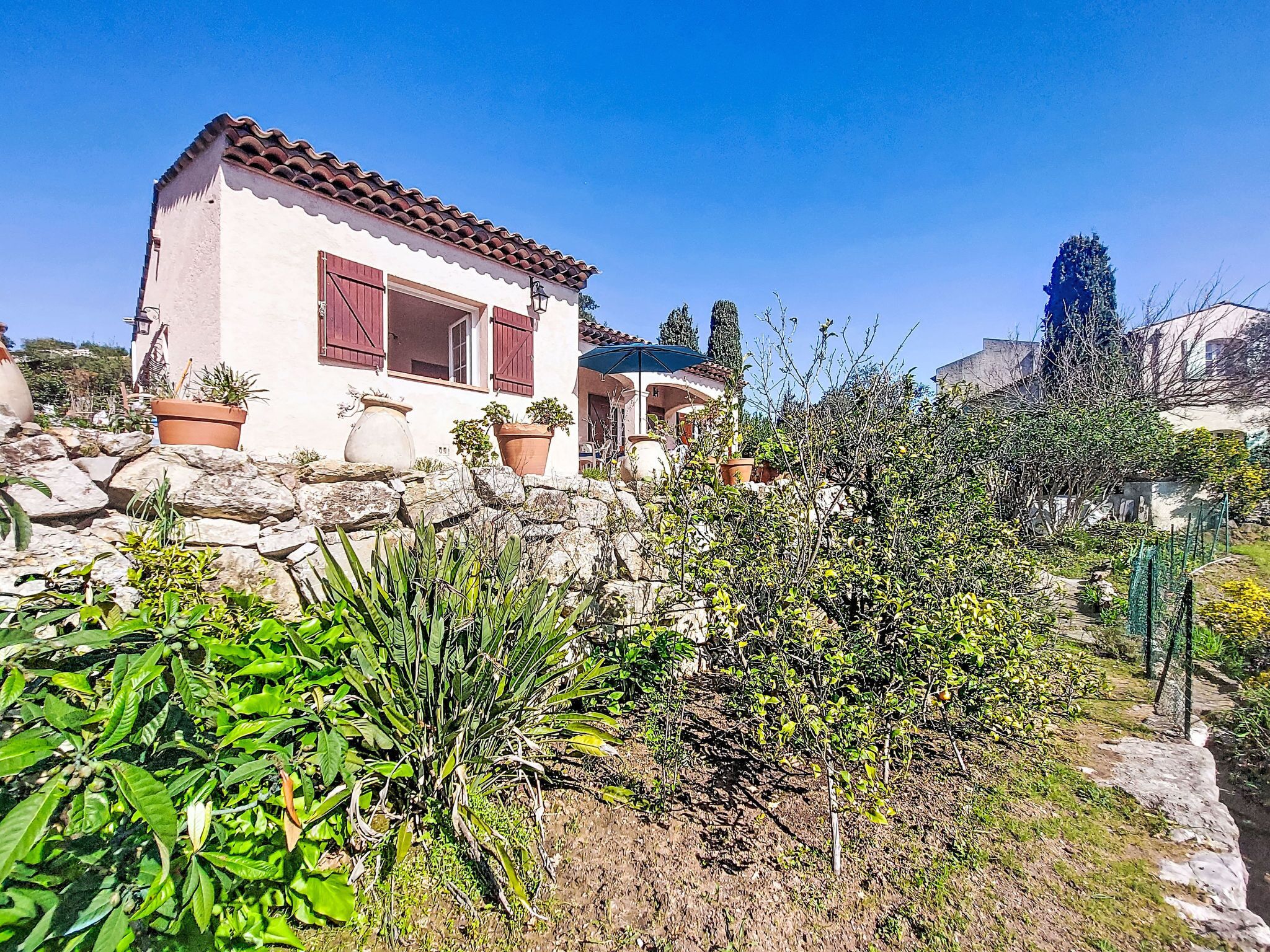 A house with a stone wall, potted plants, and a clear blue sky.