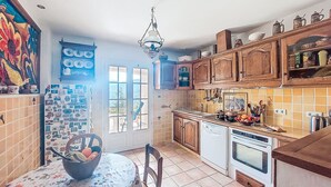 A kitchen with wooden cabinets, a tiled backsplash, a dining table with a floral tablecloth, and a view through the door. - L´Argentière by Interhome (Les Adrets)