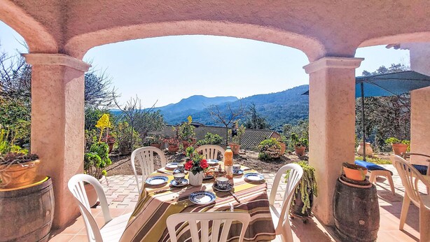 An outdoor patio with a table set for dining, surrounded by potted plants and a mountainous backdrop. - L´Argentière by Interhome (Les Adrets)