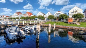 A canal with boats, a white fence, and buildings with red roofs. - Ferienwohnung Sonnenstrand Travemünde: Nähe zum Sandstrand & Ostsee-Gefühl (Lübeck)