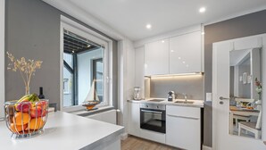 A modern kitchen with white cabinetry, a built-in oven, a coffee maker, and a fruit bowl on the counter. - Ferienwohnung Sonnenstrand Travemünde: Nähe zum Sandstrand & Ostsee-Gefühl (Lübeck)