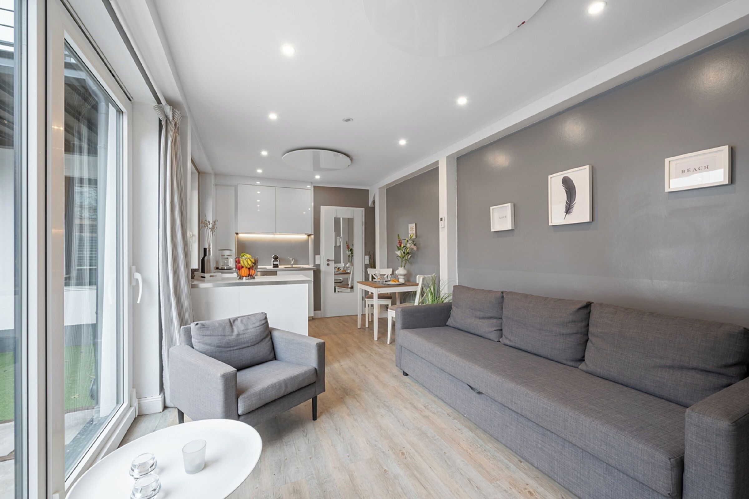 Ein modernes Wohnzimmer mit einem grauen Sofa, einem kleinen Sessel und einem Esstisch.