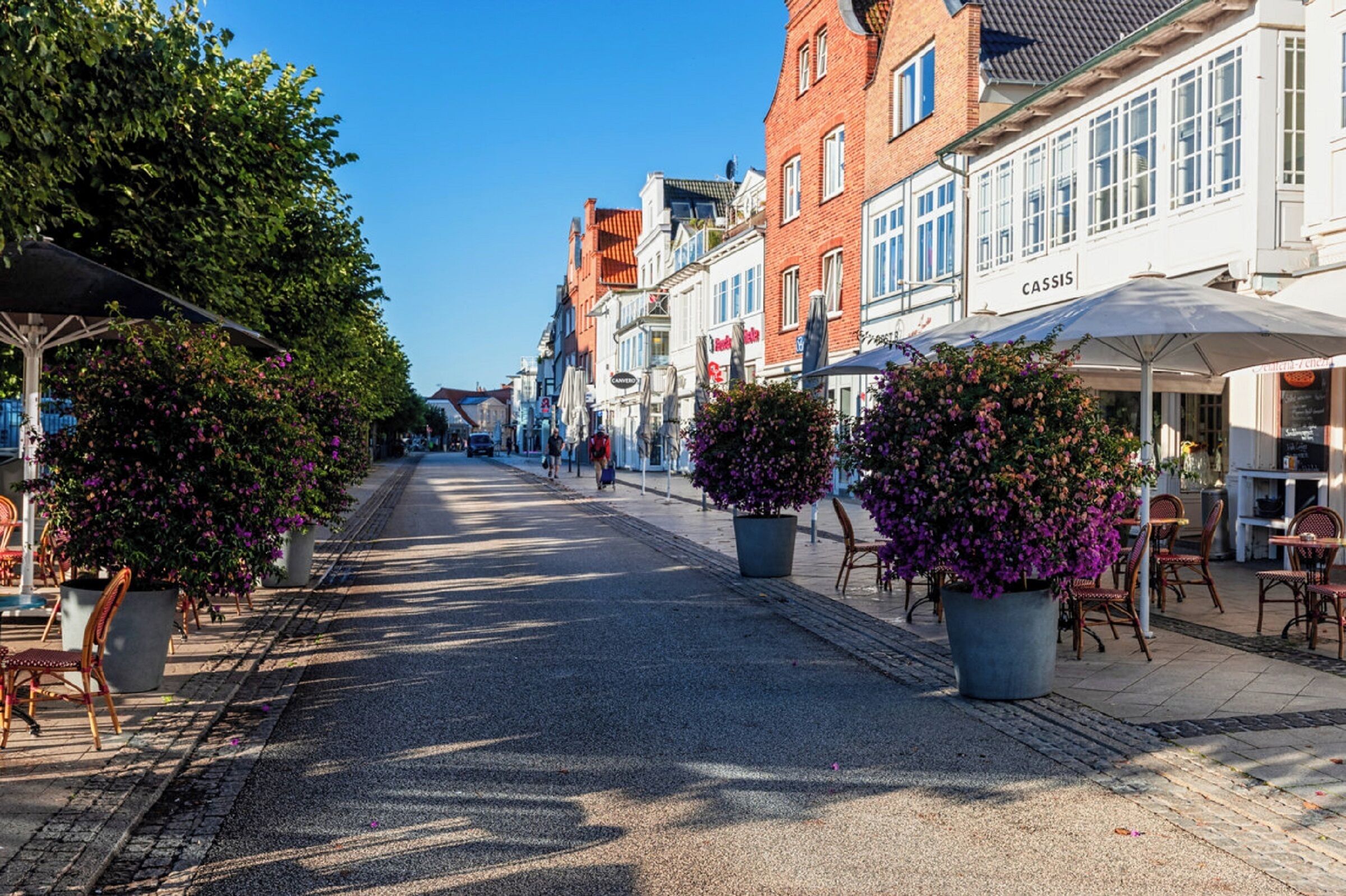 A street lined with buildings, outdoor seating, and potted plants.