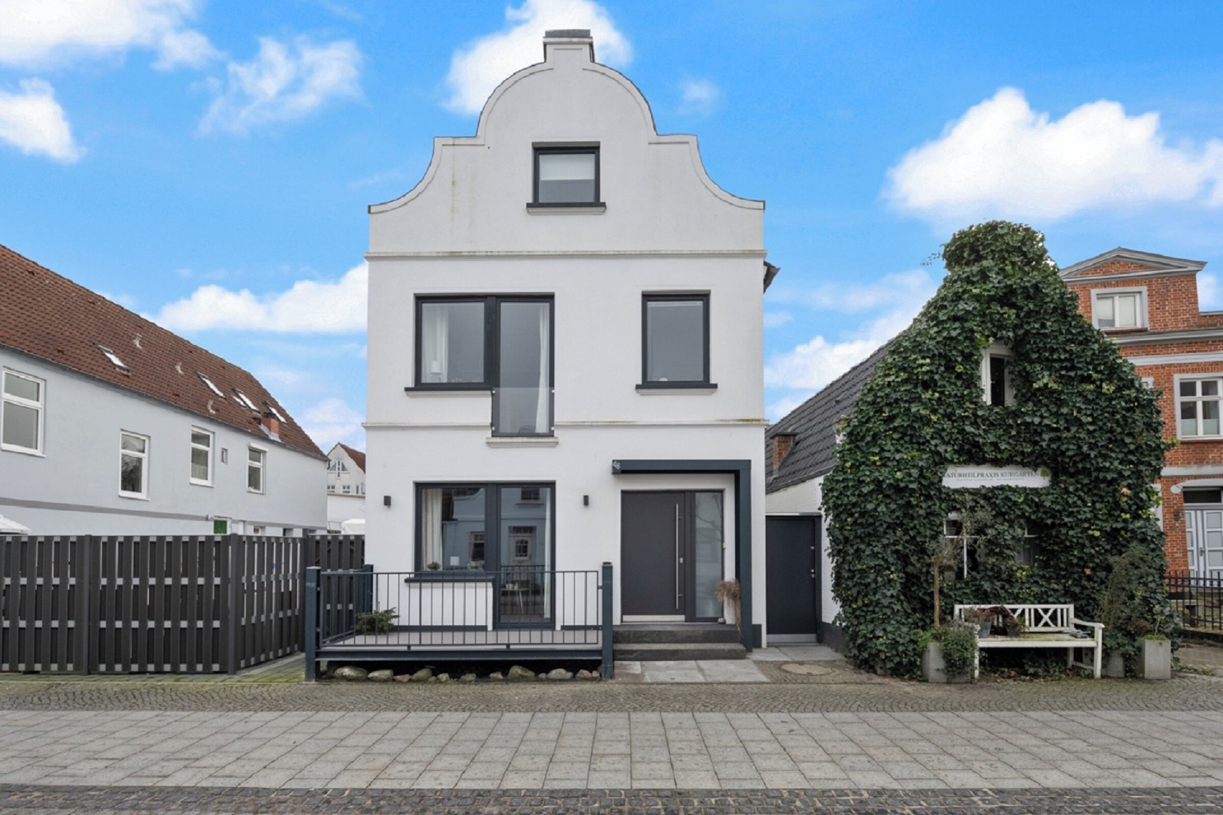 A two-story house with a white facade, a black door, and a small balcony.