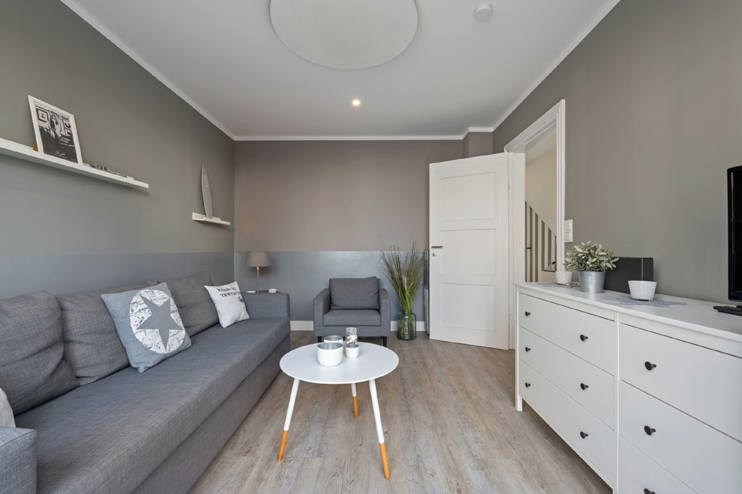 Un salon moderne avec un canapé gris, une table basse blanche et un fauteuil gris.