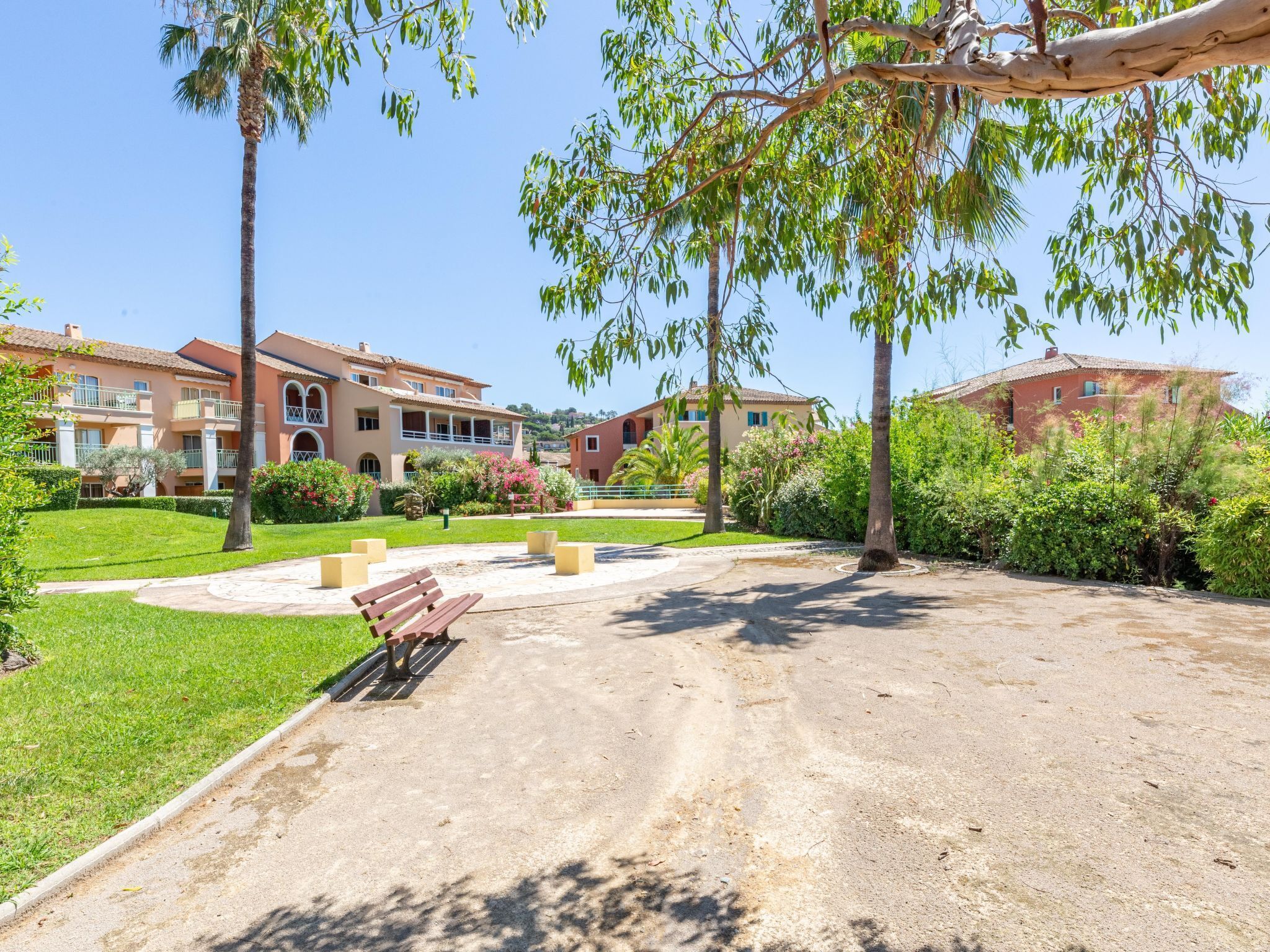 A courtyard with a bench, palm trees, and buildings with balconies.