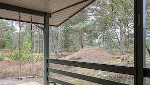 En överbyggd träveranda med en gunga, med utsikt över ett skogsområde med en grusstig och en liten kulle.