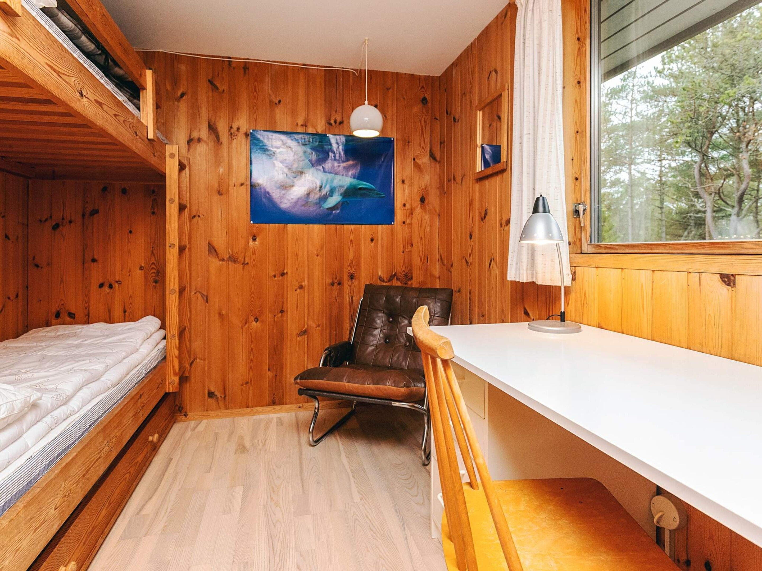 A cabin room with a bunk bed, a desk, a chair, and a window with a view of trees.