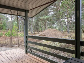 Una terraza de madera con un columpio, rodeada de un bosque de pinos.