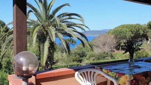 A covered outdoor area with a table, chairs, a decorative vase, and a view of the sea and hills. - Casa Roberta apartment 3 (Capoliveri isola d'Elba)