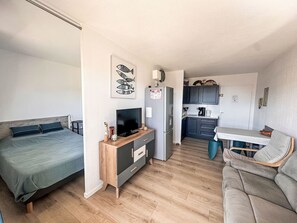 Ein kompakter Wohnbereich mit Bett, Fernseher, Küchenzeile und Essecke.