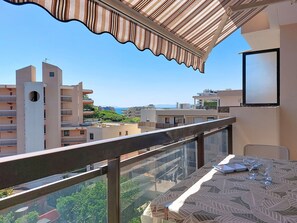 Ein Balkon mit Tisch und Stühlen, der auf einen Wohnbereich mit Gebäuden und blauem Himmel blickt.