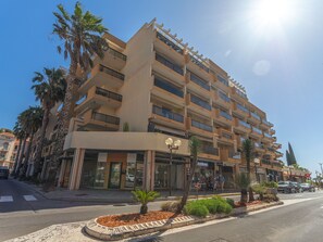 Ein mehrstöckiges Hotel mit Balkonen, einem Eingang im Erdgeschoss und Palmen im Vordergrund.