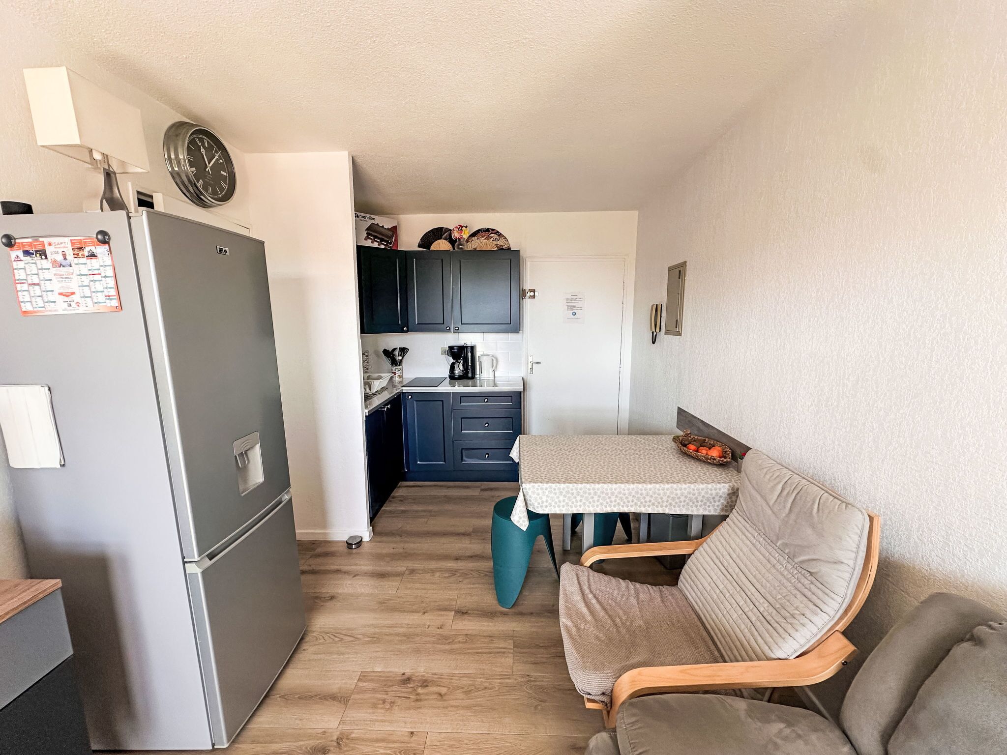 A compact kitchenette with a refrigerator, a coffee maker, and cabinets. There is a dining table with a chair and a small seating area.