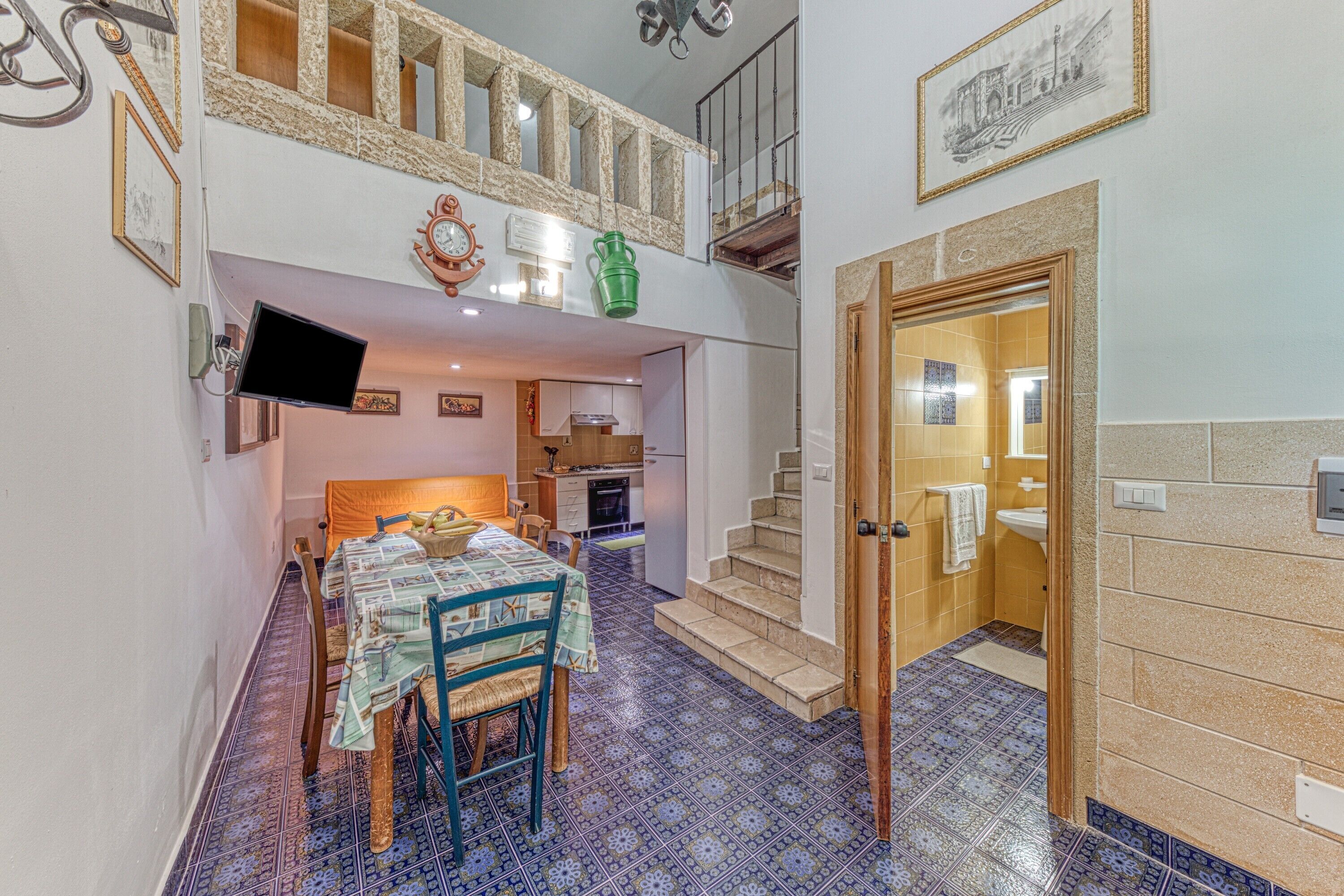 A dining area with a table and chairs, a kitchen in the background, and a staircase leading to an upper level.