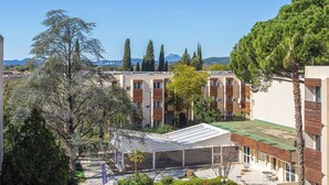 A residential area with multiple apartment buildings, a covered outdoor seating area, and a view of distant mountains. - L'île d'Or by Interhome (La Londe Les Maures)