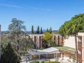 A residential area with multiple apartment buildings, a covered outdoor seating area, and a view of distant mountains. - L'île d'Or by Interhome (La Londe Les Maures)