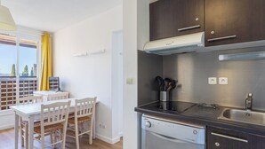 A compact kitchen with a dishwasher, dark cabinets, and a dining area with a table and chairs. - L'île d'Or by Interhome (La Londe Les Maures)