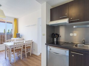 A compact kitchen with a dishwasher, dark cabinets, and a dining area with a table and chairs. - L'île d'Or by Interhome (La Londe Les Maures)