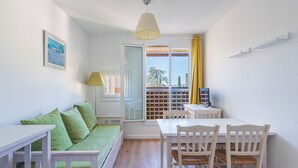 A room with a bed, a table, chairs, a lamp, a TV, and a window with a view. - L'île d'Or by Interhome (La Londe Les Maures)