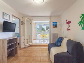 Ein Zimmer mit Fernseher, einer Couch, einem Esstisch und Blick durch eine Glastür.