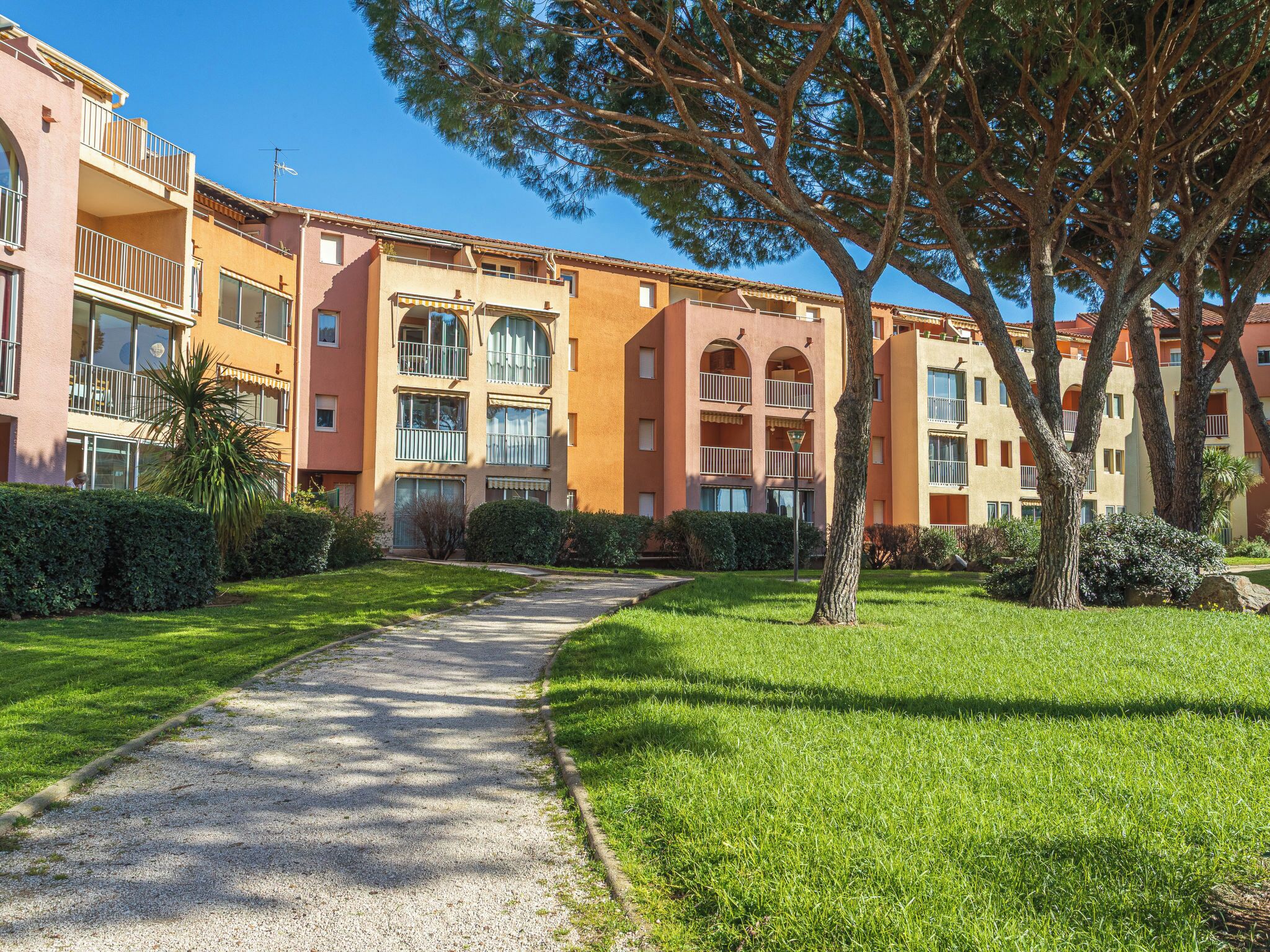 A multi-story building with balconies, a gravel pathway, and well-maintained greenery.