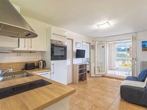 Eine kompakte Küche mit Einbauofen, Spüle und Toaster. Ein Fernseher ist an der Wand montiert, und es gibt einen Balkon mit Blick ins Freie.