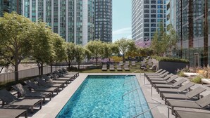 Una piscina en la azotea con sillones de descanso, rodeada de edificios altos y árboles.