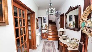Un couloir avec une porte en bois, un escalier, un lustre, un miroir et un tapis à motifs.