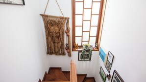 Un escalier en bois mène à une pièce dotée d’une fenêtre, d’une décoration murale en macramé et de tableaux encadrés accrochés au mur.