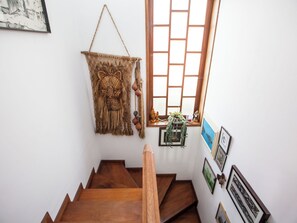 Una escalera de madera que conduce a una habitación con ventana, un tapiz de macramé y cuadros en la pared.