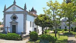 Une église blanche, dotée d’un clocher et surmontée d’une croix, entourée de jardins bien entretenus et baignée par un ciel bleu azur.