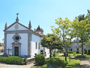 Un edificio blanco con una cruz en la parte superior, un ventanal circular y un campanario.