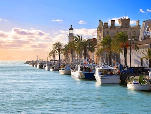 A harbor with boats docked, a historic building with a tower, and palm trees lining the waterfront. - Le Mehari by Interhome (Le Grau du Roi)