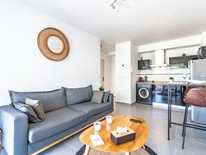 Ein modernes Wohnzimmer mit grauem Sofa, einem Couchtisch und einer Küchenzeile inklusive Waschmaschine.