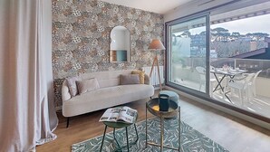 A modern living room with a patterned wallpaper, a sofa, a coffee table, a floor lamp, and a large window with a city view. - Maris Stella by Interhome (Arcachon)