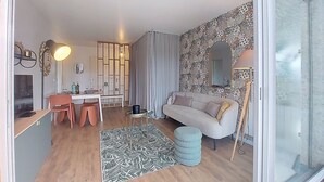 A modern living room with a sofa, a dining table with chairs, a patterned rug, and a large window. - Maris Stella by Interhome (Arcachon)