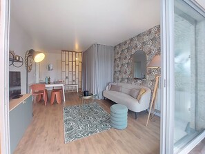 Ein modernes Wohnzimmer mit einer Couch, einem Esstisch mit Stühlen, einem gemusterten Teppich und einem großen Fenster.