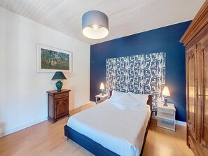 Un dormitorio con cama, dos mesitas de noche, una lámpara, un cuadro en la pared y un armario.